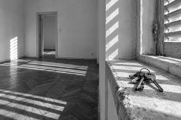 Un trousseau de clés posé sur l’appui de fenêtre d’un appartement vide, les lames d’un volet rayant le sol d’ombres dures.